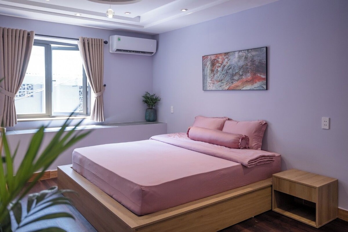 Un dormitorio moderno con cama, una mesita de noche pequeña, una planta en maceta y una ventana con cortinas.