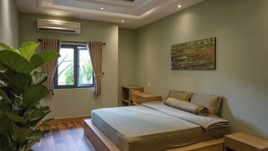 A bedroom with a large bed, wooden headboard, a bedside table, a nightstand, a window with curtains, and a potted plant. - Ben Thanh Homestay And Apartment (Ho Chi Minh Municipality)