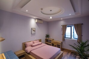Ein Schlafzimmer mit Bett, Schreibtisch, Stuhl, einem Fenster mit Vorhängen und einer Deckenleuchte.