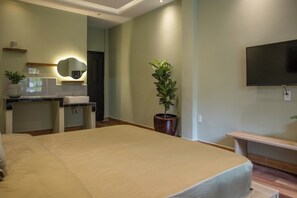 Hotelkamer met een groot bed, een bureau met stoel, een wastafel, een spiegel, een potplant en een aan de muur bevestigde televisie.