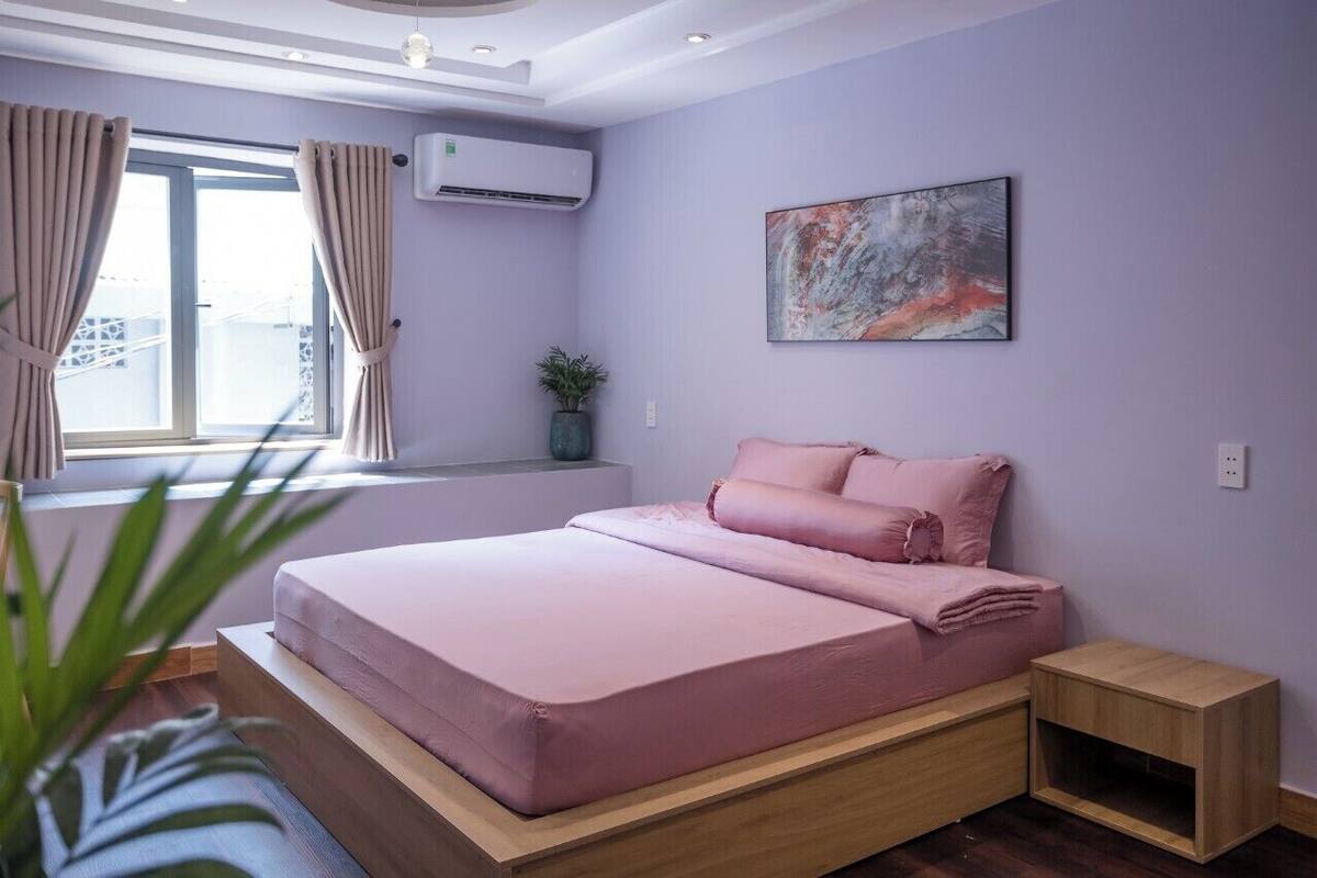 A modern bedroom with a bed, a small bedside table, a potted plant, and a window with curtains.