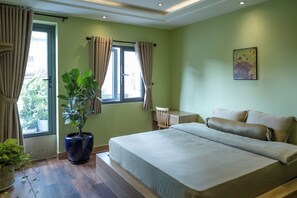 Ein Schlafzimmer mit einem großen Bett, einer Topfpflanze, einem Schreibtisch und einem Fenster mit Vorhängen.
