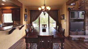 A spacious dining area with a long wooden table, dark wooden chairs, and a chandelier.