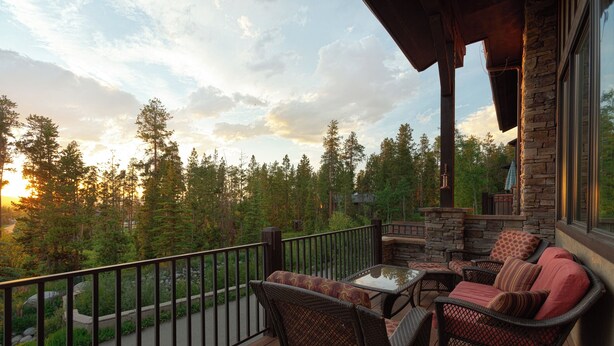 A wooden deck with outdoor furniture, a stone wall, and a view of a forest.