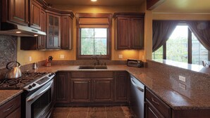 A kitchen with dark wood cabinets, granite countertops, a built-in stove, and a window with a view of greenery.