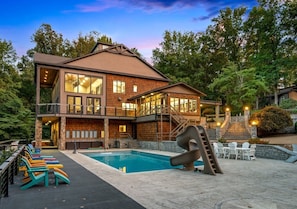 Une maison à deux étages avec une piscine, un espace salon extérieur et un toboggan.