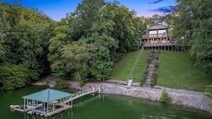 A lakeside property with a dock, a covered boat launch, and a house with a large balcony.
