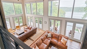 A spacious living room with a large brown leather sectional sofa, a wooden coffee table, and a glass door leading to a deck.
