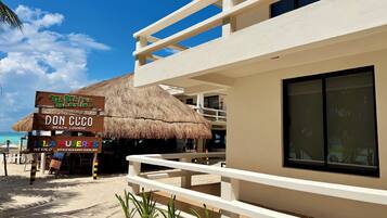 A beachfront hotel with a thatched roof, a sign for 'Don Cuco Beach Lounge', and a view of the ocean.