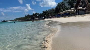 A beach with clear water, palm trees, and beach umbrellas.