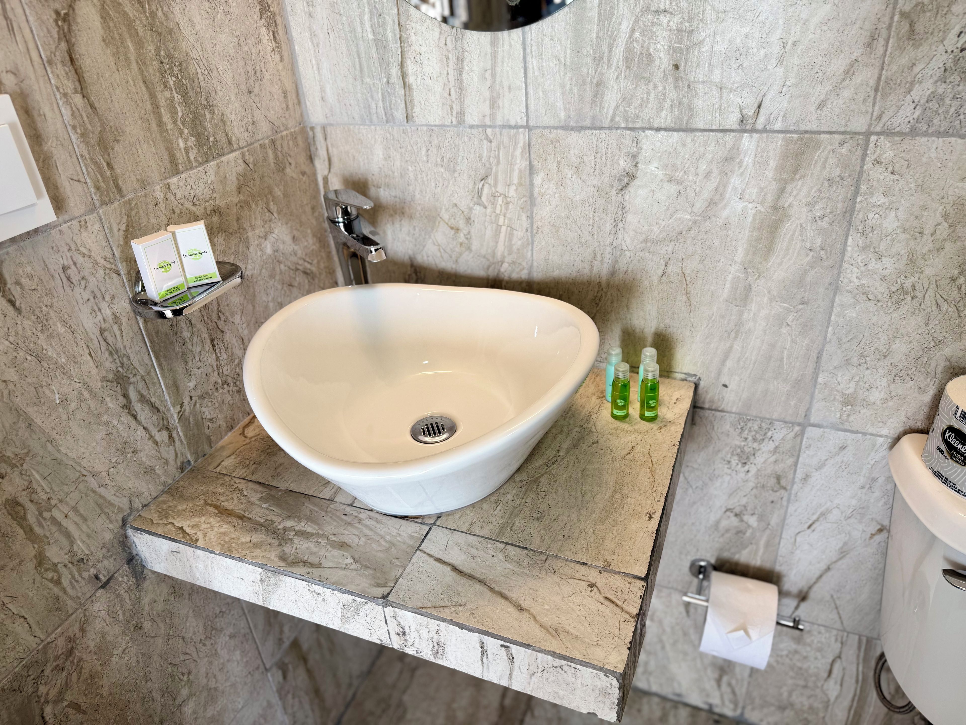 A bathroom with a white sink, a mirror, a towel dispenser, and a toilet.