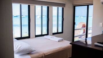 A hotel room with a bed, a desk, and a view of the ocean through large windows.