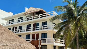 A multi-story hotel with balconies, a thatched roof, and palm trees.