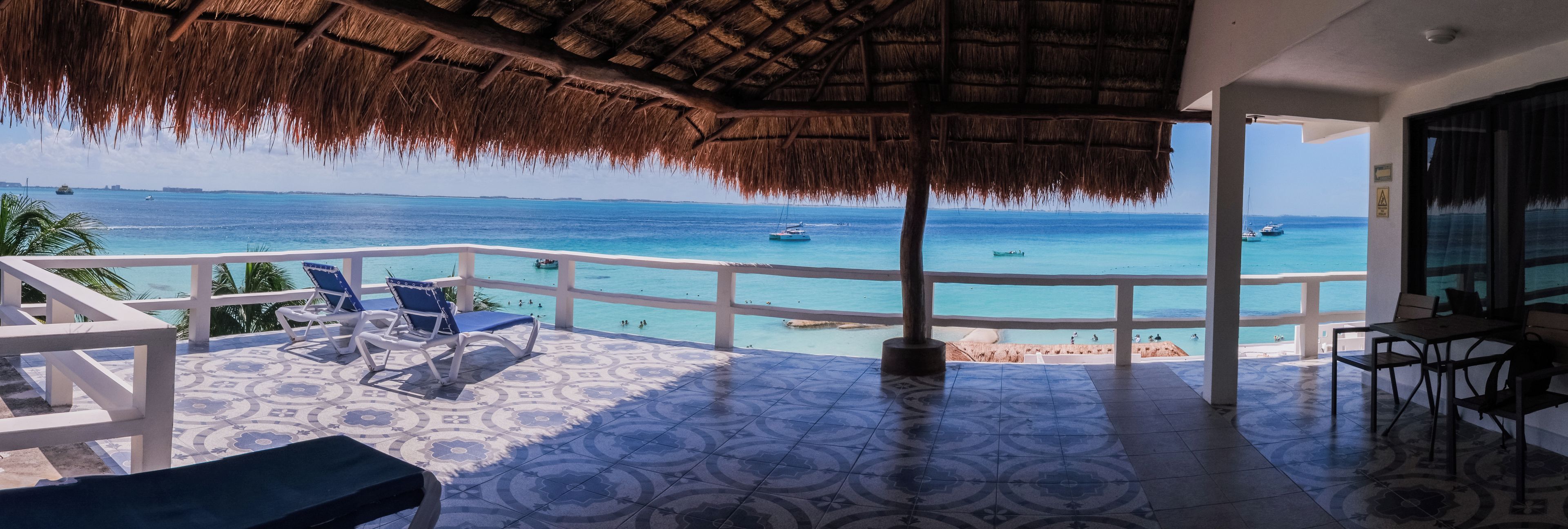 A balcony with a thatched roof, overlooking a turquoise sea with boats.