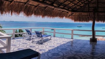 A balcony with a thatched roof, overlooking a turquoise sea with boats.