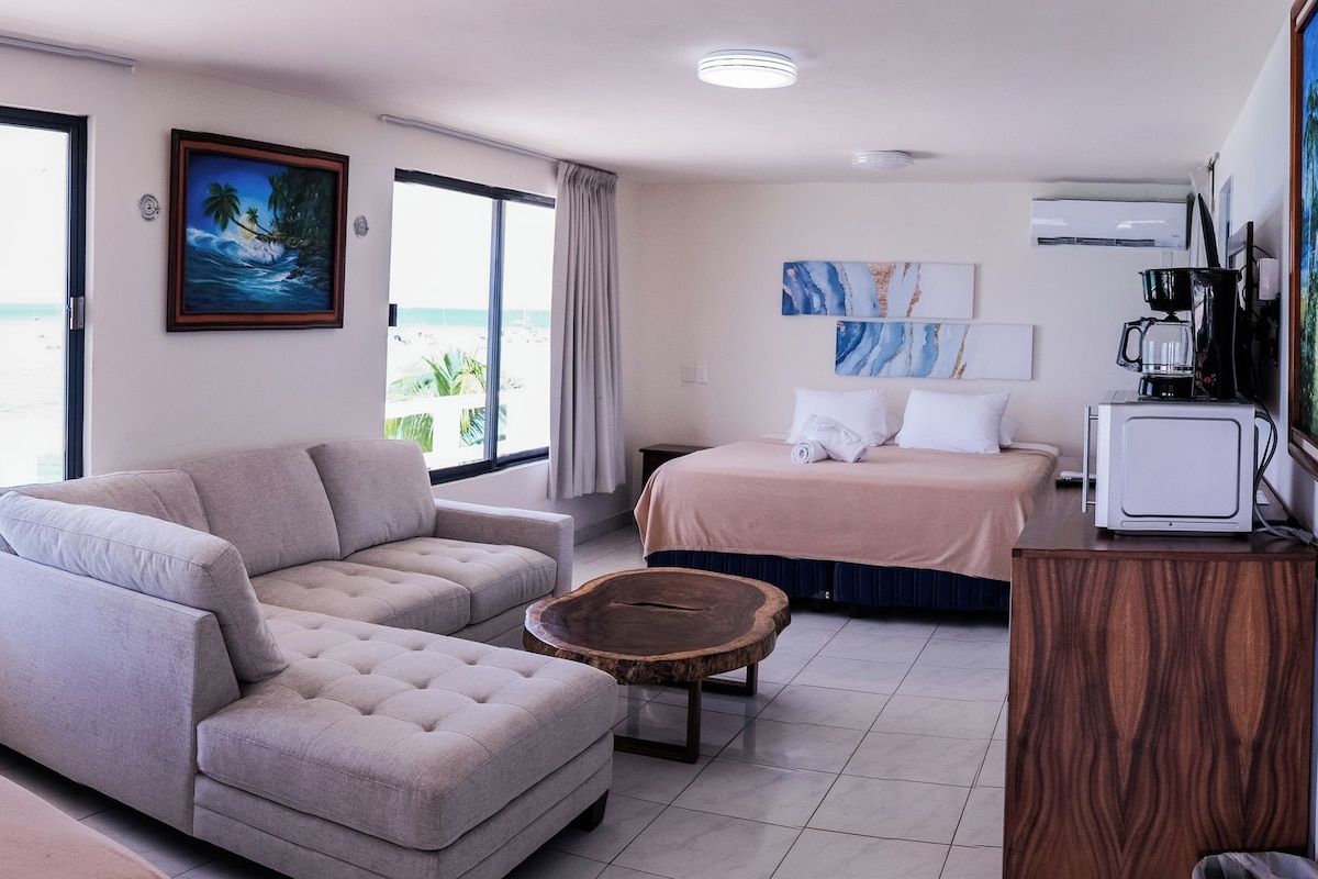 A hotel room with a sofa, a bed, a small table, and a view of the beach.