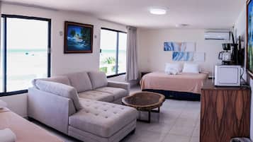 A hotel room with a sofa, a bed, a small table, and a view of the beach.
