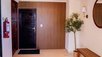 A wooden door, a fire extinguisher, a potted plant, a bench, and a wall-mounted lamp.
