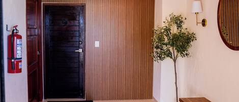 A wooden door, a fire extinguisher, a potted plant, a bench, and a wall-mounted lamp.