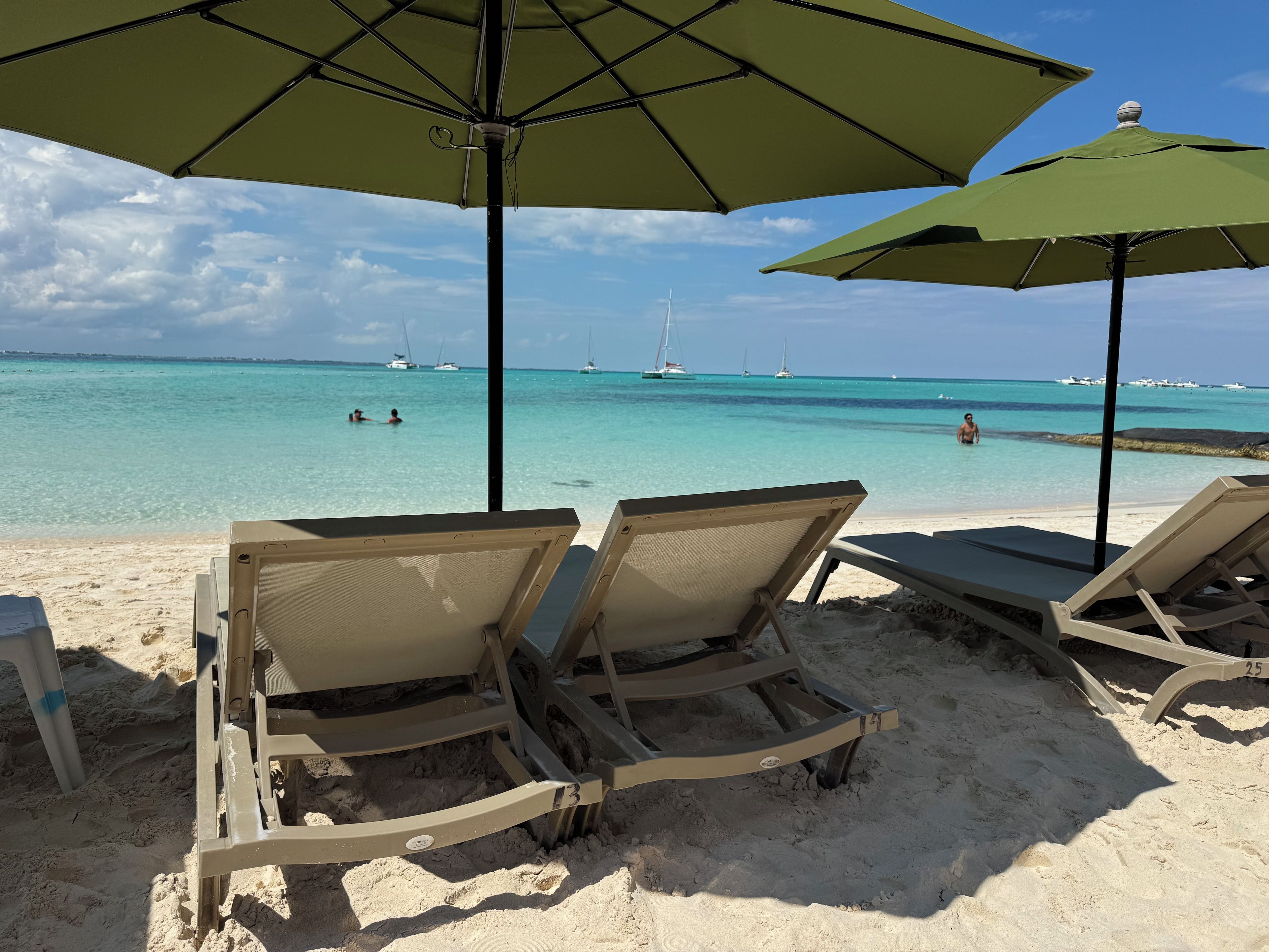 A beach with lounge chairs and umbrellas, a clear view of the ocean, and sailboats in the distance.