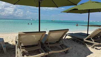 A beach with lounge chairs and umbrellas, a clear view of the ocean, and sailboats in the distance.