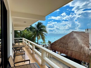 A balcony with wooden chairs and a thatched-roof structure. - Chichis and Charlies (Isla Mujeres)