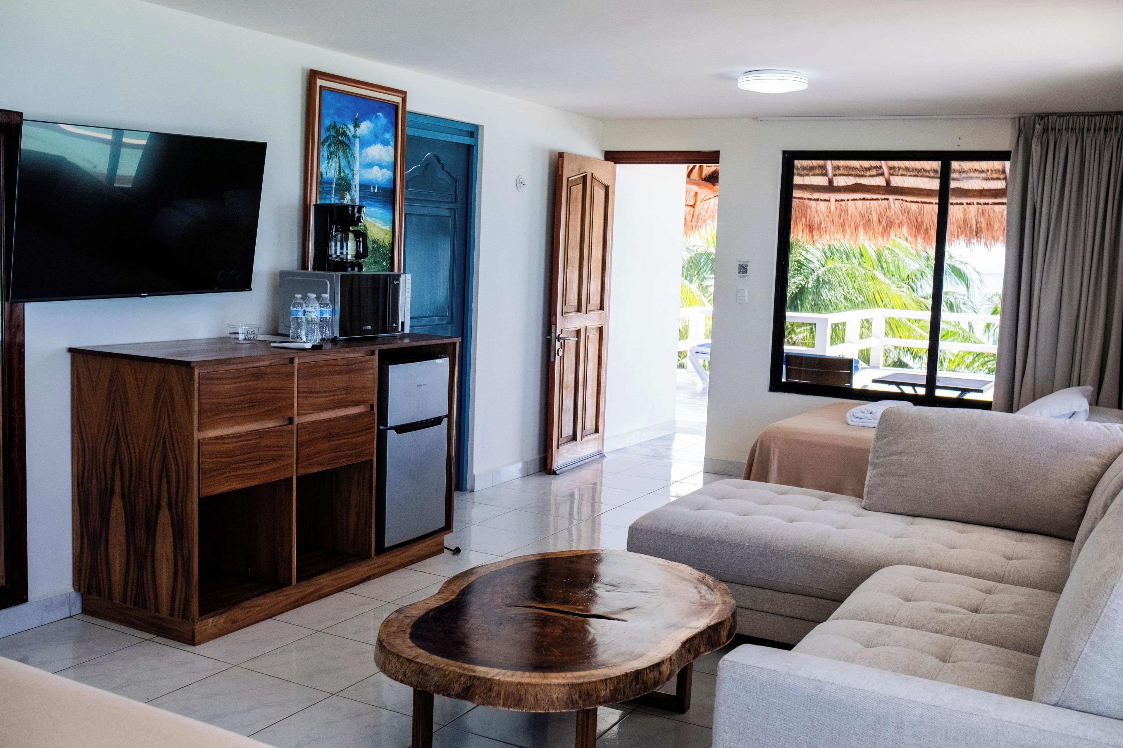 Uma sala de estar moderna com televisão de tela plana, móveis de madeira, um sofá e vista para uma varanda com telhado de palha.