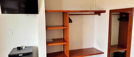 A room with a built-in wooden shelving unit, a television mounted on the wall, and a small table with a power outlet.