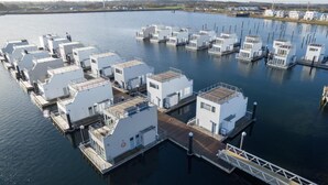 A marina with multiple docked boats, each with a white cabin structure, connected by walkways. - Awesome ship in Olpenitz with sauna (Olpenitz)
