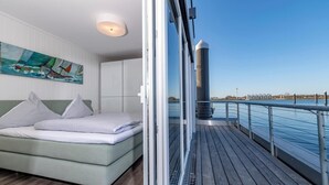 A modern room with a bed, a painting, and a view of the water. - Awesome ship in Olpenitz with sauna (Olpenitz)