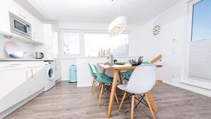 A modern kitchen with white cabinets, a microwave, a washing machine, and a dining area with a table and chairs. - Awesome ship in Olpenitz with sauna (Olpenitz)