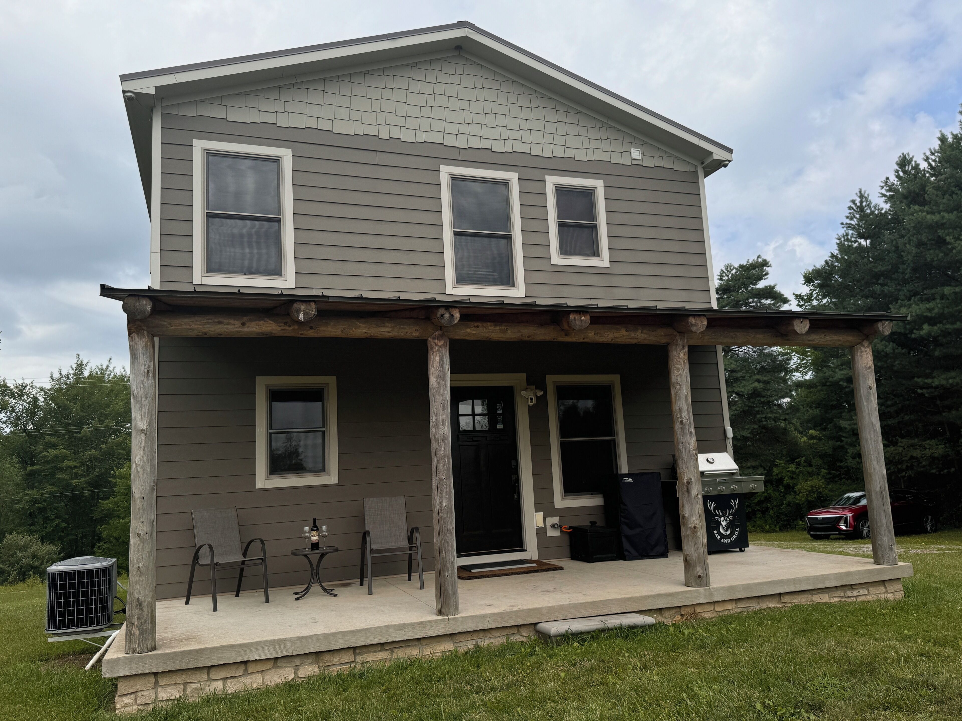 A two-story house with a porch, a small table with chairs, and a grill.
