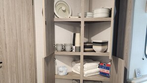 Un meuble en bois doté d’étagères où sont rangées des assiettes, des bols et des serviettes.