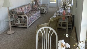 Un salon chaleureux avec un canapé à motifs floraux, une table basse en verre, un fauteuil en osier et un ventilateur de plafond.