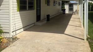 Un espace extérieur abrité, avec un chemin en béton menant à un bâtiment doté d’un porche.
