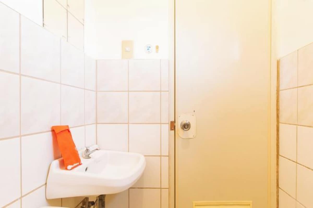 Un bany amb rajoles blanques, un lavabo i una tovallola taronja penjada a la paret.