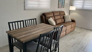 Een zithoek met een houten tafel en stoelen, een bruine bank en een lamp.