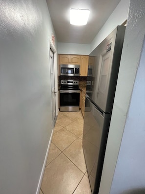 A narrow kitchen with a refrigerator, stove, microwave, and oven.