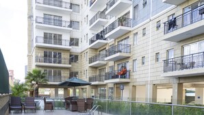 Una piscina con bordes de azulejos, rodeada por una valla baja, y contigua a un edificio residencial de varios pisos con balcones.