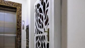 Un pasillo con un ascensor moderno y una puerta blanca decorativa con diseños de hojas.