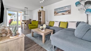 Ein modernes Wohnzimmer mit einem grauen Sofa, einem Holztisch und einem Essbereich mit Tisch und Stühlen.