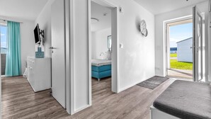 Ein moderner, gut beleuchteter Raum mit Holzboden, einem Bett mit grauem Topper, einem blau gepolsterten Kopfteil und einem weißen Kleiderschrank.
