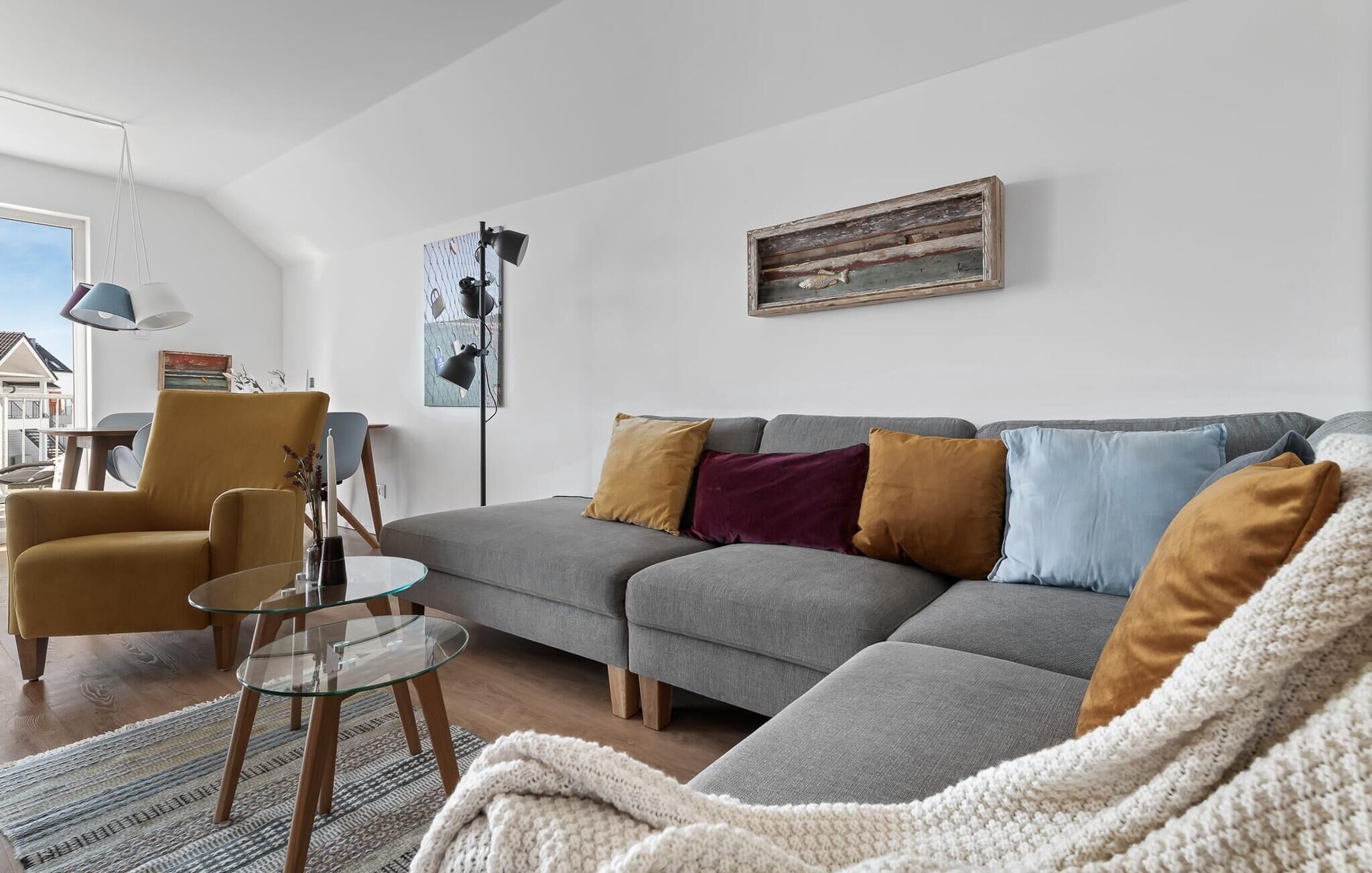 A modern living room with a grey sectional sofa, a yellow armchair, a glass coffee table, and a knitted throw.