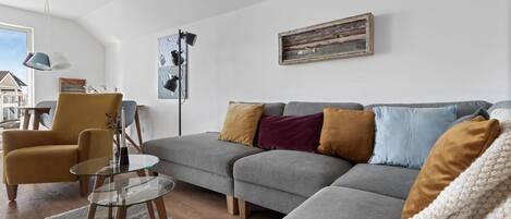 A modern living room with a grey sectional sofa, a yellow armchair, a glass coffee table, and a knitted throw.