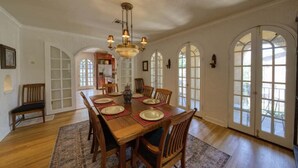 A dining room with a wooden table set for six, surrounded by chairs, with a chandelier above. - Italian Villa next to Gathering Place with pool (Tulsa)
