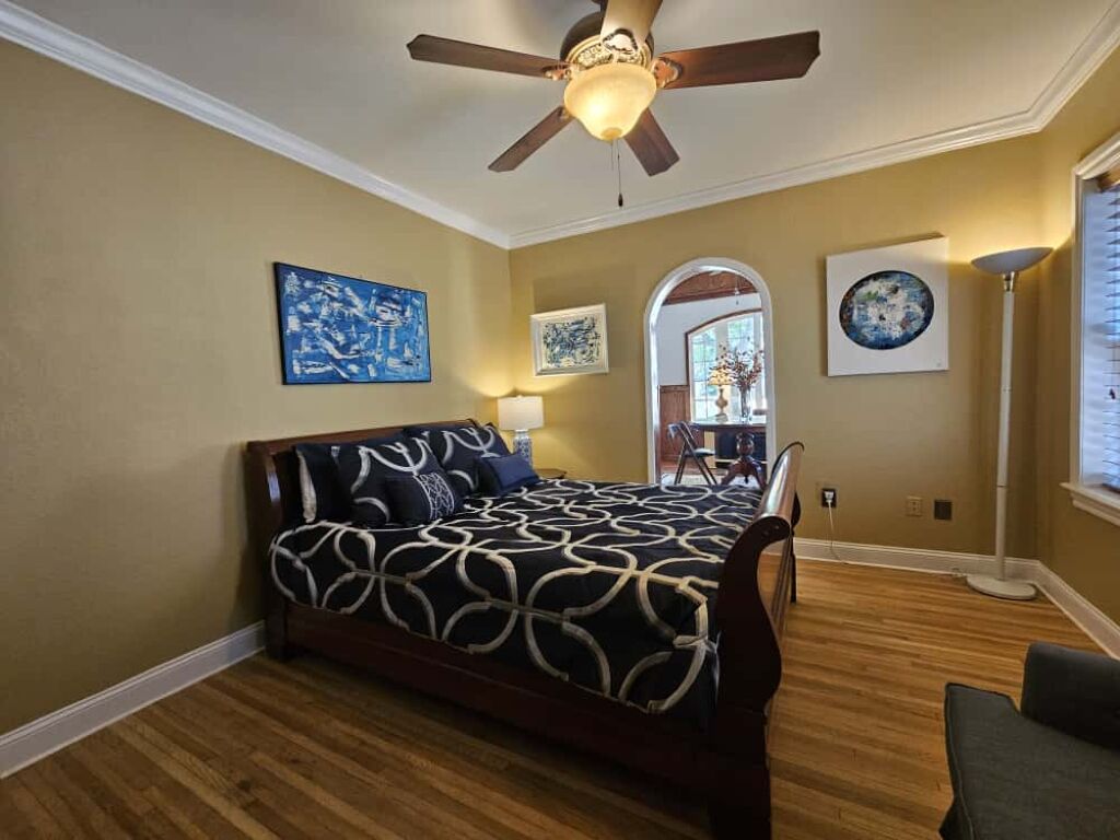 Ein Schlafzimmer mit einem Bett, einem Deckenventilator und Kunstwerken an den Wänden.