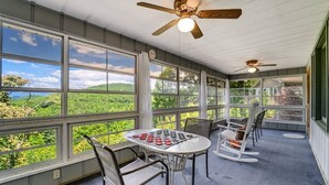 A covered porch with a table and chairs, large windows with a view of greenery, and ceiling fans.