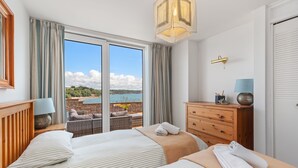 A hotel room with two beds, a wooden dresser, a lamp, and a view of the outdoors. - Captains View - Sea and Harbour Views Parking (Saundersfoot)