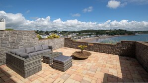 A patio with a wicker sofa, a small table, and a potted plant. - Captains View - Sea and Harbour Views Parking (Saundersfoot)