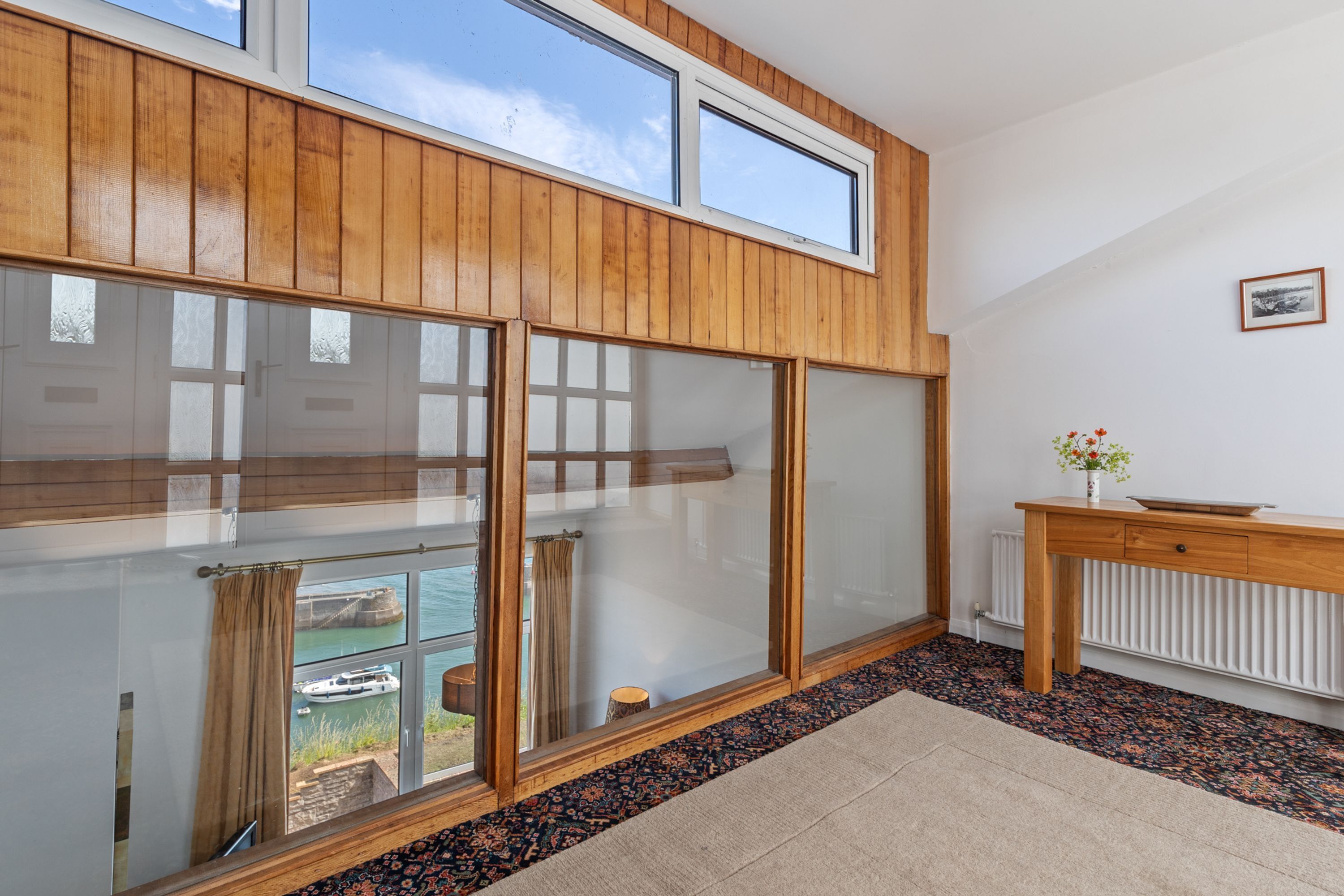 A room with large windows, a wooden ceiling, a radiator, and a small table with a vase.